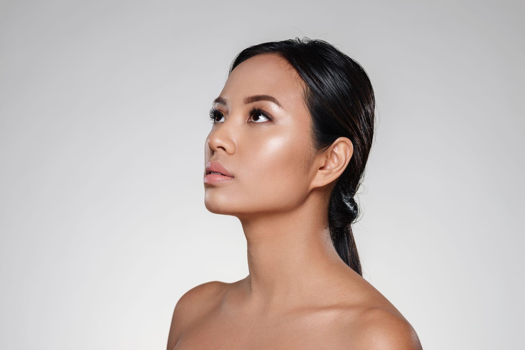 Side-profile portrait of a woman with dark hair pulled back, bare shoulders, against a neutral gray background.