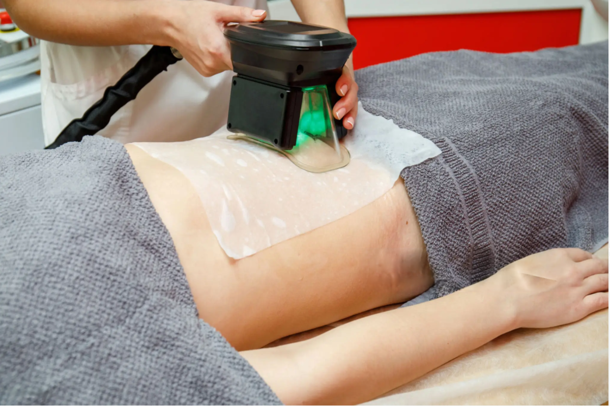 Therapist uses a handheld light therapy device on a patient’s lower back with a gel pad and green light.